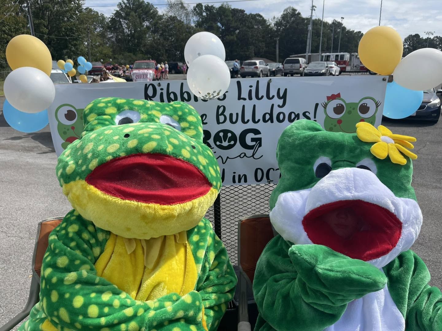 Ribbet and Lilly with balloons in front of their festival sign